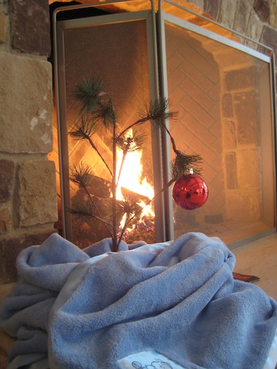 charlie brown tree with blue blanket around bottom by fireplace